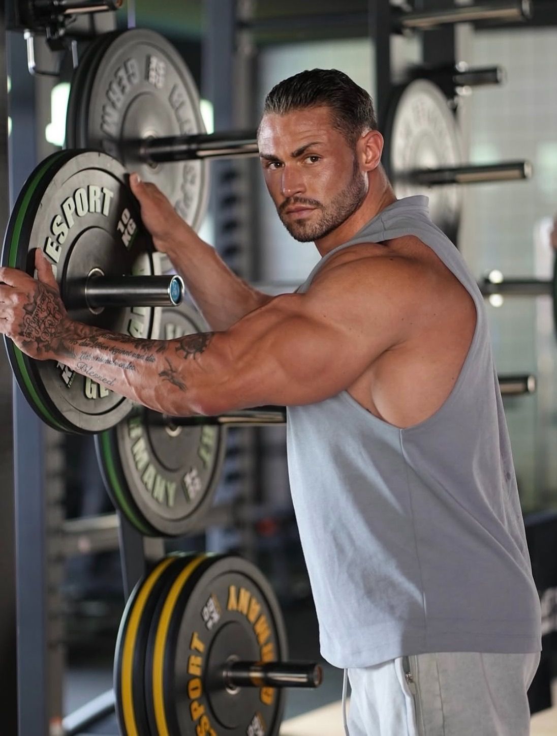 Der Coach steht an einem Hantelständer im Fitnessstudio und hält eine Hantelscheibe.